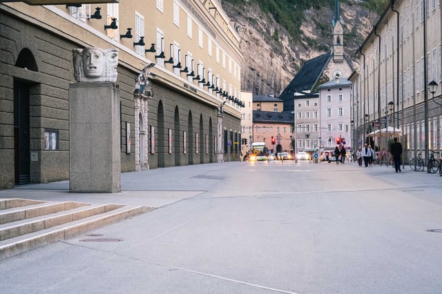 Hofstallgasse with Festspielhaus colonnade and Moenchsberg cliff face in Salzburg old town.