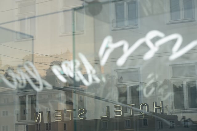 Hotel Stein storefront window reflects Altstadt buildings and distant Festungsberg silhouette in Salzburg