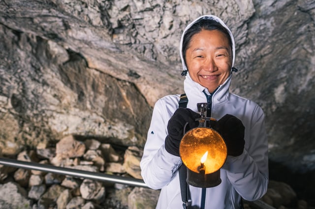 Hyunok Jang, hood up and gloved, smiles while holding a lit carbide lamp before the Eisriesenwelt cave tour.
