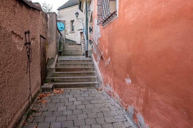 Narrow alley of the Imbergstiege with stone steps between salmon and beige walls in the Salzburg old town