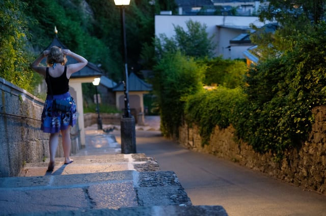Stone steps of the Imbergstiege descending from the Kapuzinerberg into the old town in evening light with a person walking down past a small wall shrine and lit lantern