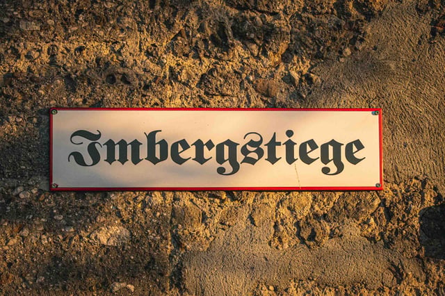 Enamel street sign reading Imbergstiege in blackletter font mounted on rough stone in Salzburg.