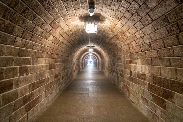 The long vaulted stone tunnel that runs from the Kehlstein bus stop to the Eagle's Nest lift, two small figures silhouetted at the bright far end.