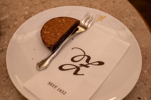 Close view of a slice of chocolate-dipped Zaunerstollen with a silver cake fork, resting on a white napkin printed with the Zauner monogram and the words SEIT 1832.