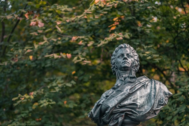 Close-up of the bronze Mozart bust surrounded by autumn foliage on Kapuzinerberg in Salzburg.
