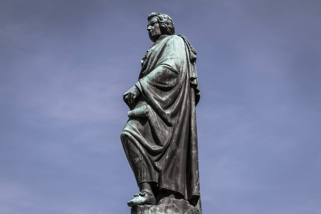 Bronze Mozart statue silhouetted against a pale blue sky on Mozartplatz in Salzburg old town