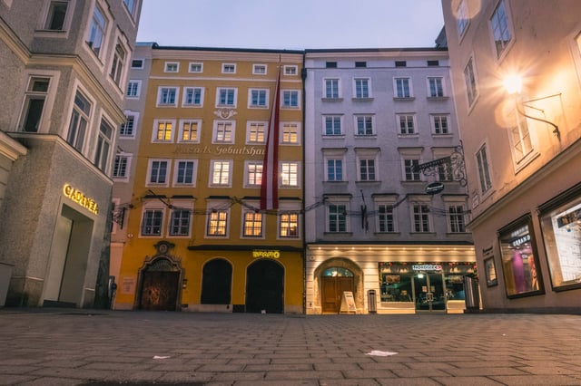 The yellow Mozart Birthplace on Getreidegasse with Austrian flag at twilight in Salzburg old town