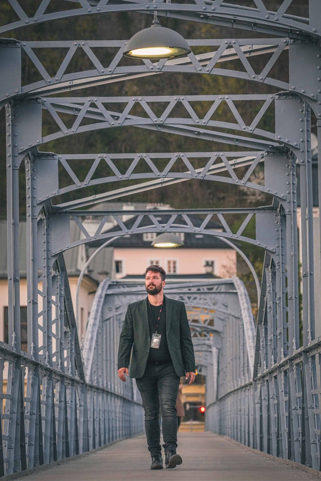 Man walks along the steel-arched pedestrian deck of Mozartsteg bridge in Salzburg.