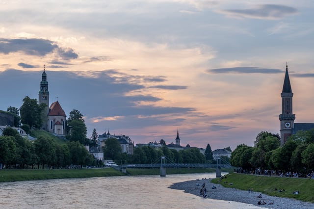 Mulln Church on the left and Christuskirche spire on the right flank the Salzach river at dusk in Salzburg.