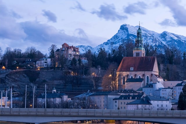 Mülln Church and hillside villas glow at dusk with Untersberg rising behind in Salzburg.