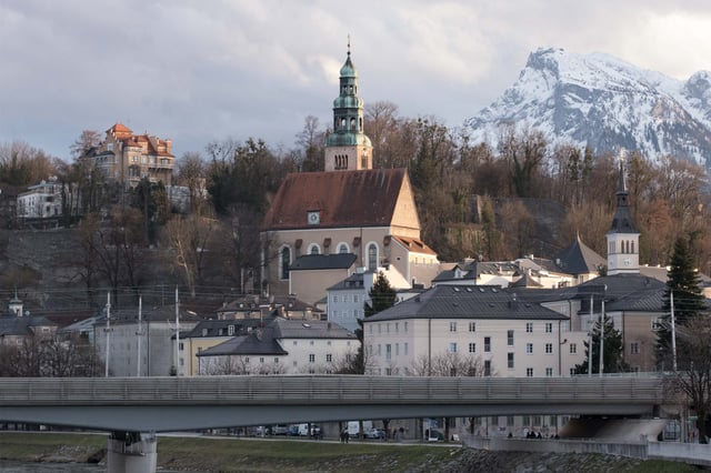 Mülln Church with its distinctive tower stands before the snow-capped Untersberg in Salzburg.
