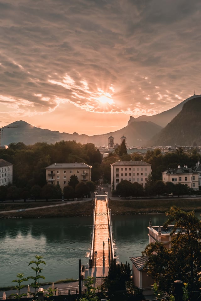 Footbridge Muellnersteg crosses the Salzach at sunrise with Gaisberg and Kapuzinerberg beyond.