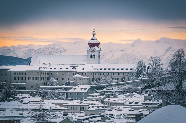 Nonnberg Abbey with snowy Alps behind at sunset seen across the Salzburg rooftops.