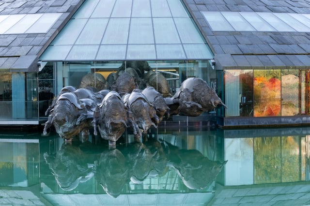 Close view of the bronze bulls breaking out through the glass facade of the Red Bull headquarters and wading into the green water, their reflections directly beneath them.