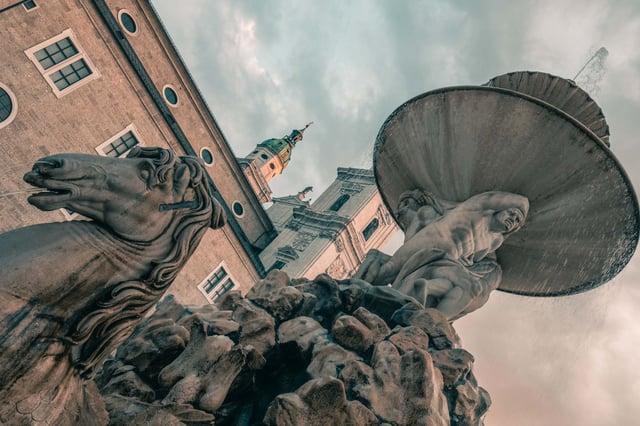 Horse and triton figures of the Residenzbrunnen fountain with Michaelskirche tower behind in Salzburg.