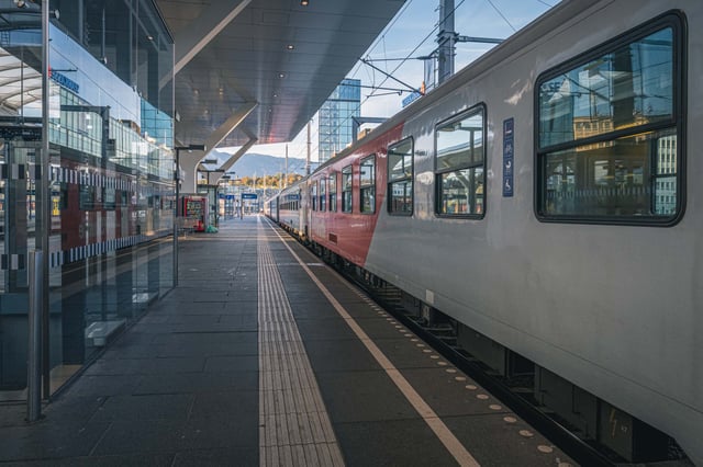Modern glass canopy over a platform with a red train at Salzburg Hauptbahnhof.
