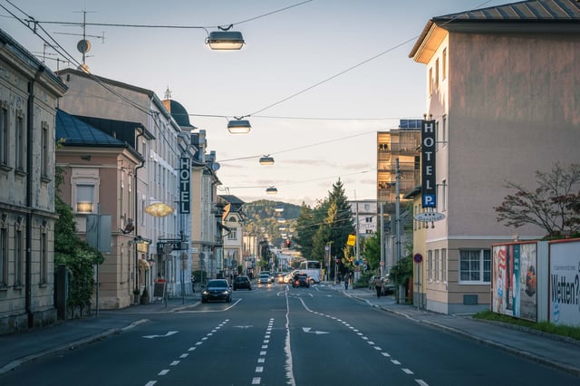 Hotel signs line a quiet Neustadt street at dusk with the Kapuzinerberg visible in Salzburg.