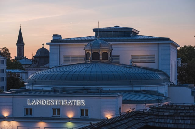 Salzburger Landestheater building with central dome and illuminated sign at dusk in Salzburg