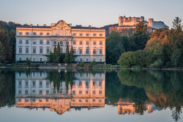 Schloss Leopoldskron reflected in Leopoldskroner Weiher with Hohensalzburg fortress at sunset
