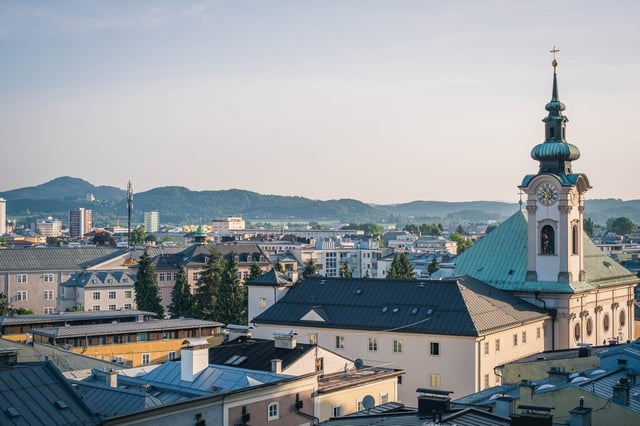 Sebastianskirche tower rising above Salzburg Neustadt rooftops with hills behind