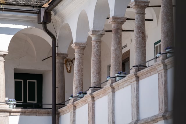 The arcaded upper gallery of the Renaissance courtyard at Seeschloss Ort, with rough marble columns, flower boxes on the rail, a mounted skull and the doorway to the Wappensaal.