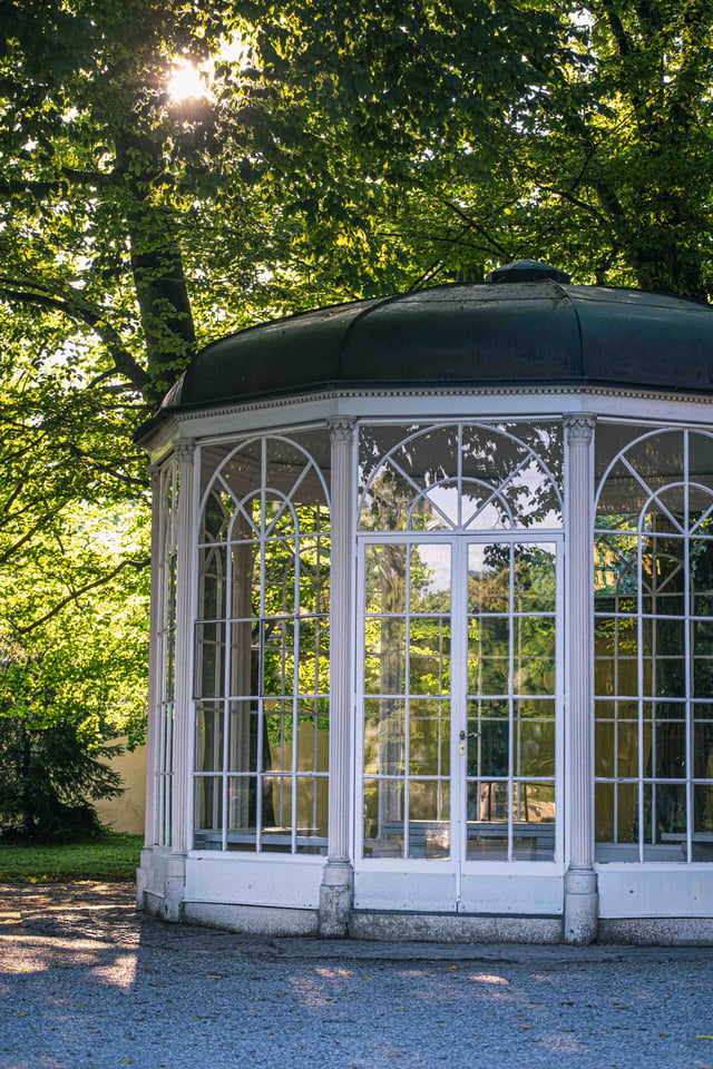 Sound of Music glass pavilion backlit by sunlight through trees at Hellbrunn in Salzburg.