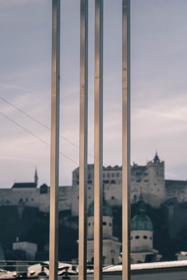 Vertical metal rods of the Spirit of Mozart piece frame Hohensalzburg Fortress and cathedral domes in Salzburg.