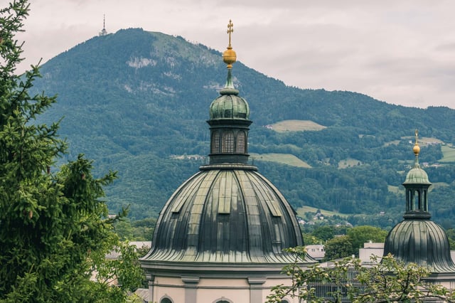 The ribbed copper dome of the Erhardkirche in Nonntal with golden cross and a smaller flanking turret with the Gaisberg and its TV mast in the distance