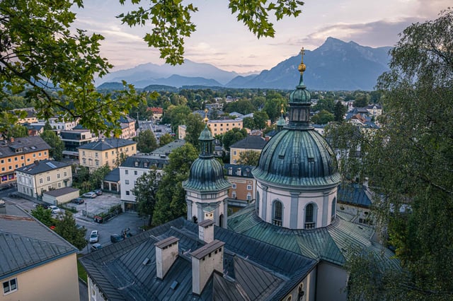 Green dome of Erhardkirche rises above Nonntal rooftops with Untersberg behind in Salzburg.