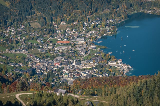 St. Gilgen seen steeply from above in autumn, the village packed around its church spire with sailing boats moored off the harbour on the Wolfgangsee.