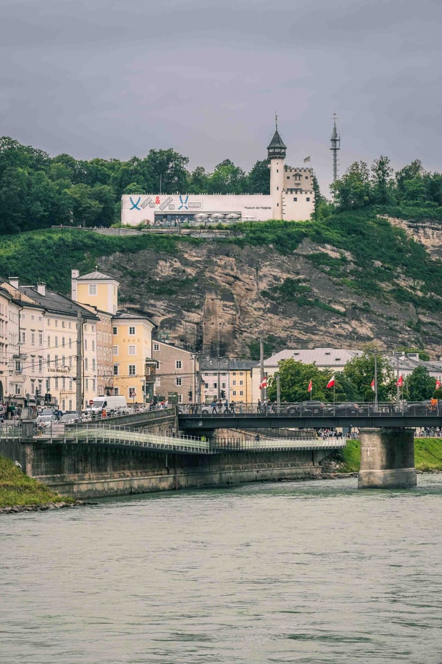 The Staatsbrucke crosses the Salzach with the Monchsberg lift and Museum der Moderne above in Salzburg.