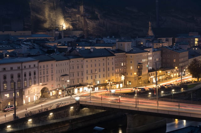 Staatsbrücke at night with car light trails and the Mönchsberg rock wall behind in Salzburg.