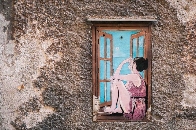 Painted mural of a woman at a window on a weathered wall on Steingasse in Salzburg.