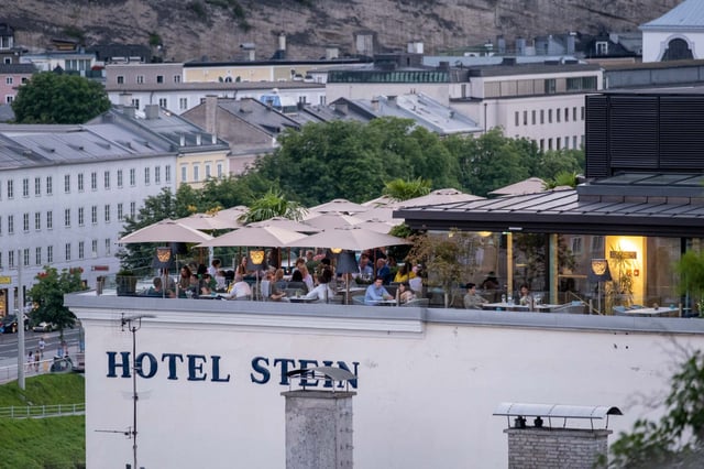 Steinterrasse rooftop bar of Hotel Stein with diners and umbrellas overlooking Salzburg rooftops.