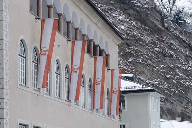 Stiegl beer flags hang from the Stieglkeller facade against the snowy Festungsberg cliff in Salzburg.
