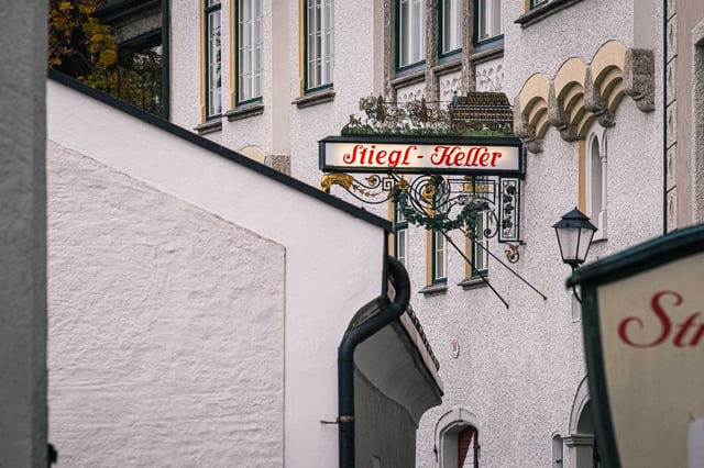 Ornate wrought iron Stiegl-Keller sign with golden horn hanging above a Salzburg alleyway.