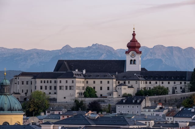 Nonnberg Abbey complex with its distinctive red-capped clock tower above Salzburg rooftops and the northern Alps beyond