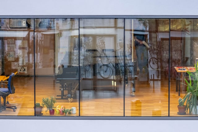 Grand piano and bicycle visible through the glass facade of a ground-floor studio at the Universitaet Mozarteum building in Salzburg-Mirabellplatz