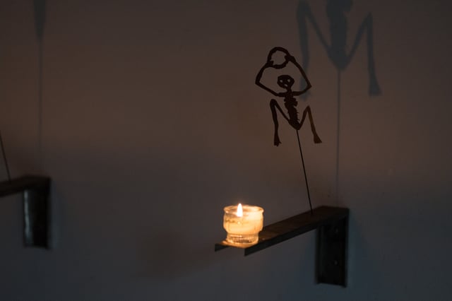 A single candle on a small wall bracket throws the enlarged shadow of a cut-metal skeleton figure across the wall of the crypt beneath Salzburg Cathedral.