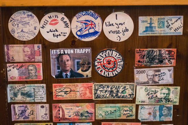 Collage of guest stickers and banknotes on the wall of the YoHo hostel bar in Salzburg.