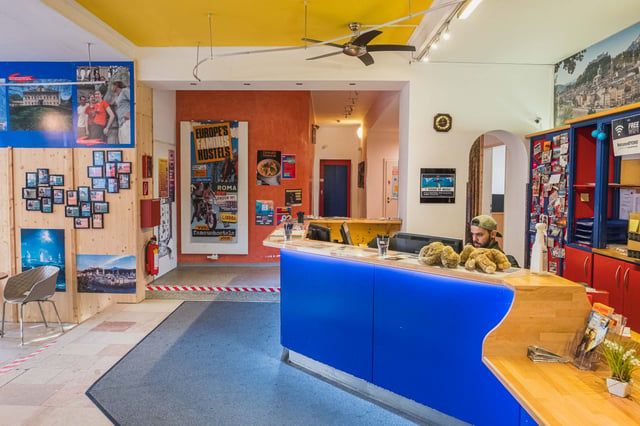 Colourful reception desk with a staff member and travel posters inside YoHo Hostel in Salzburg