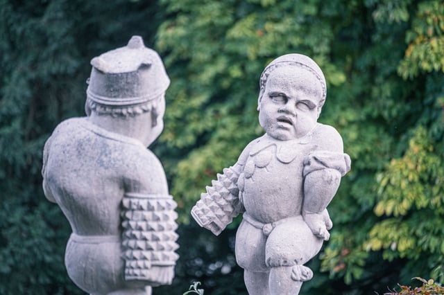 Two carved marble dwarf sculptures with armour and chubby features in Zwerglgarten Salzburg