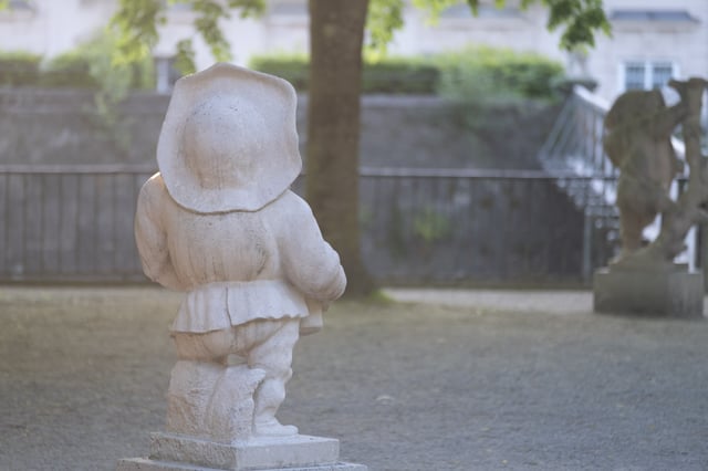 Carved marble dwarf statue with wide brimmed hat in Zwerglgarten dwarf garden in Mirabell Gardens.