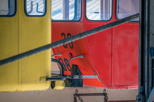 A yellow and a red riveted single-seat cable car cabin stand nose to nose inside the station, their hulls crossed by a steel haul rope.